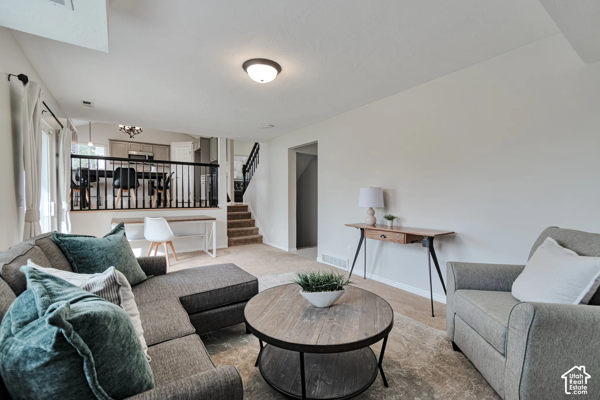 Split-level interior featuring neutral wall tones, carpeted flooring, a raised area with black metal railing, and staircase with wooden handrails