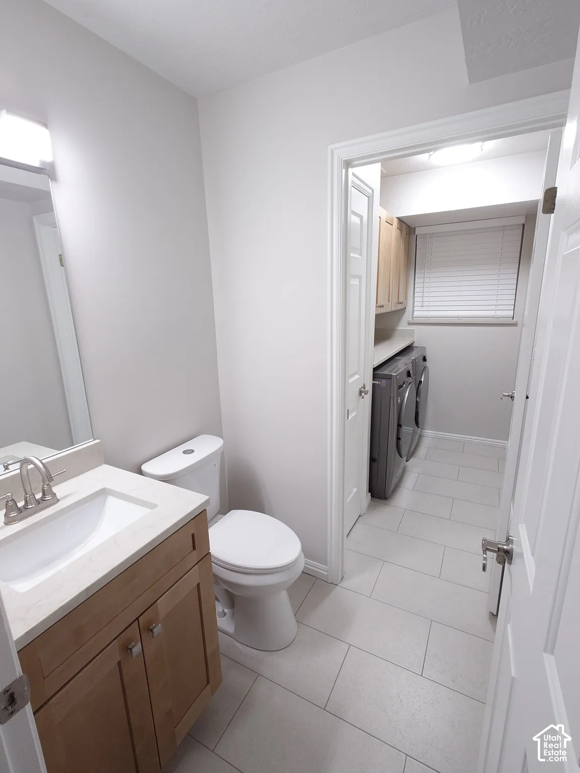 Bathroom featuring a vanity with light-tone wood cabinetry, a solid surface countertop, and an undermount sink, complemented by neutral tile flooring