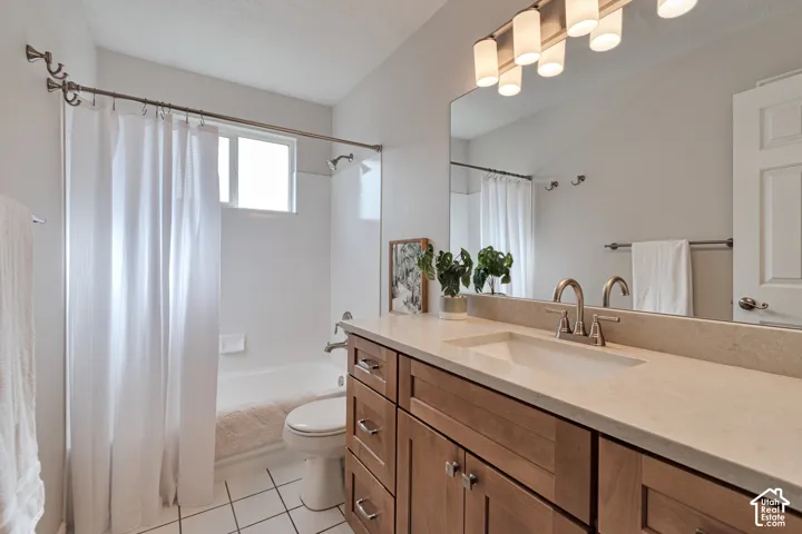 Bathroom featuring wood-finish cabinetry, neutral-toned solid surface countertop, undermount sink, multi-light fixture, and tub-shower combination with tile flooring