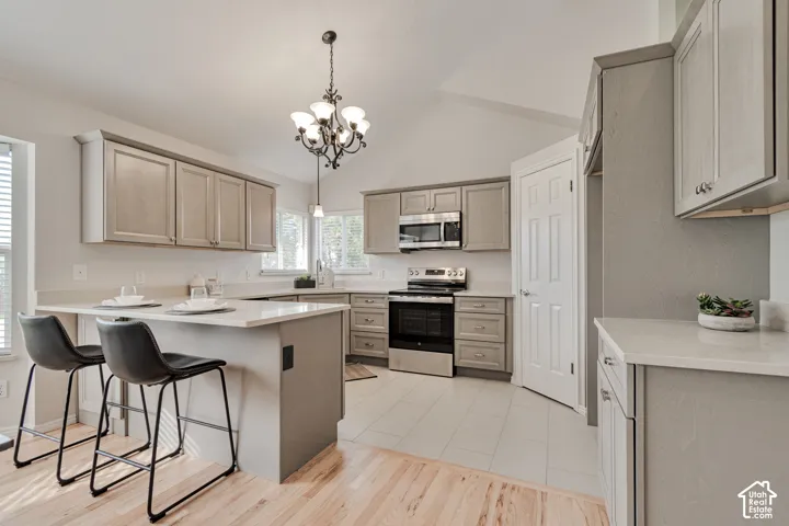 Kitchen featuring grey shaker-style cabinetry, quartz countertops, stainless steel appliances, a vaulted ceiling, and wood-finish flooring
