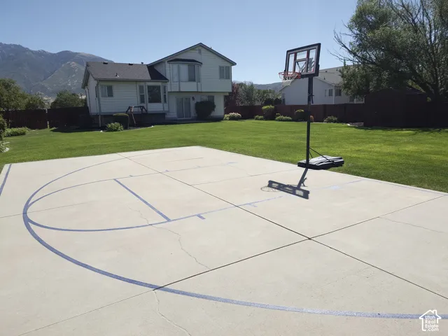 Expansive backyard featuring a concrete sports court, manicured lawn, perimeter wood fencing, and a mountain backdrop