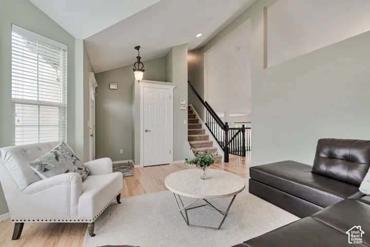 Vaulted ceilings, wood-finish flooring, staircase with a black metal railing, pendant lighting, and neutral wall tones