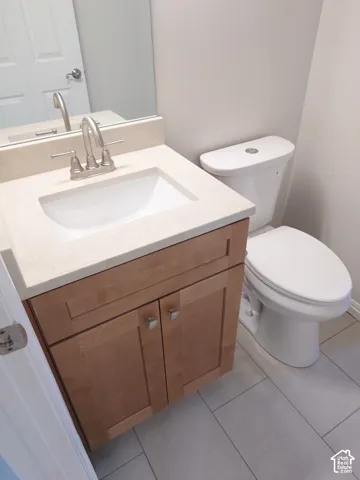Vanity featuring light wood-finish cabinetry, an integrated stone-composite countertop with an undermount basin, a brushed-nickel widespread faucet, and large-format tile flooring