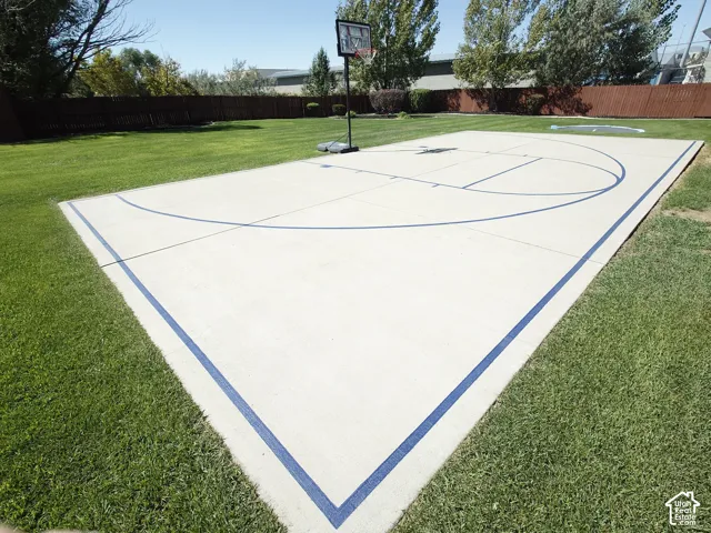Concrete basketball court featuring painted lines, surrounded by a manicured lawn and perimeter wood fencing