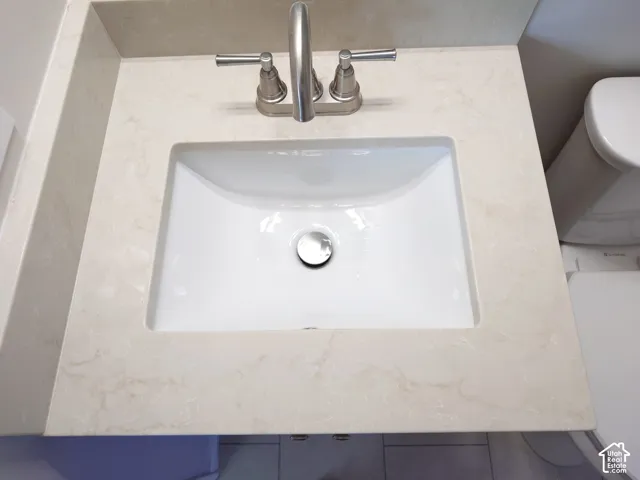 Neutral-toned countertop with an integrated backsplash, undermount rectangular basin, and brushed nickel widespread faucet
