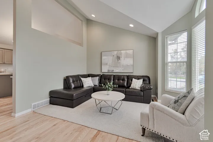 Vaulted ceilings, wood-finish flooring, recessed lighting, and large windows with horizontal blinds