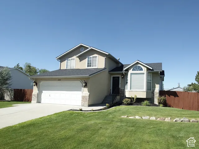 Split-level exterior featuring a combination of stucco and stone veneer siding, an attached two-car garage, a prominent bay window, and a fenced-in yard with stone landscaping borders