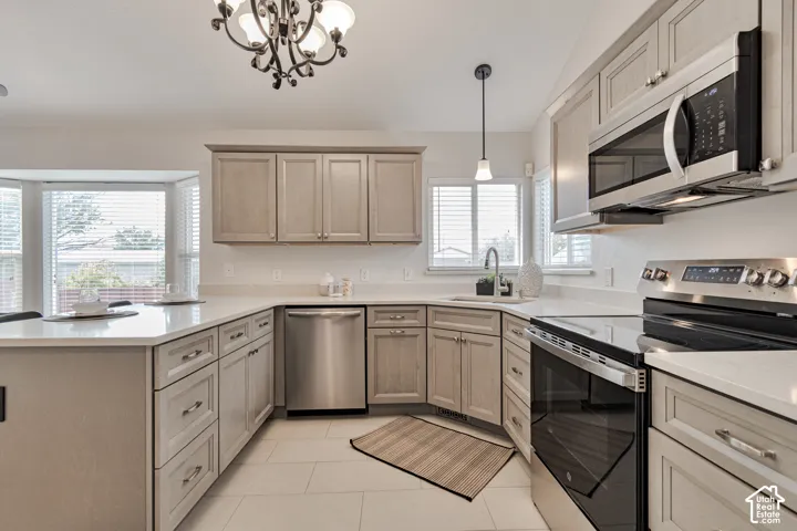 Kitchen featuring shaker-style cabinetry, quartz countertops, tile flooring, stainless steel appliances, and a wrought iron chandelier