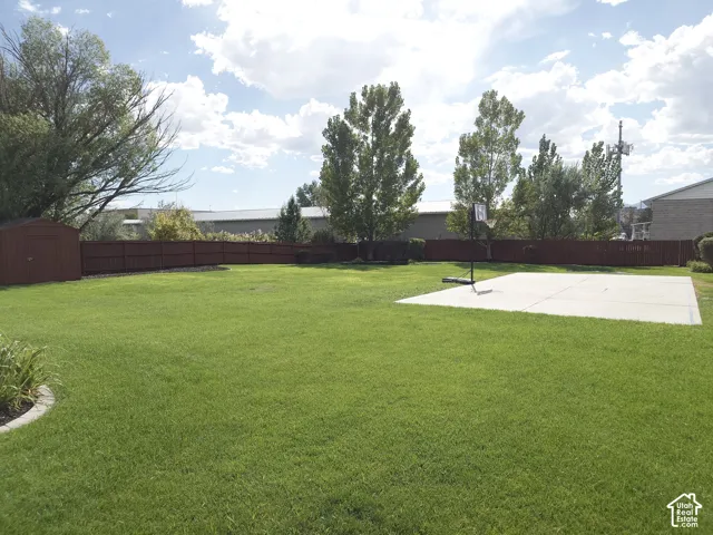 Backyard featuring a grass lawn, perimeter wood fencing, concrete sport court, and detached storage shed