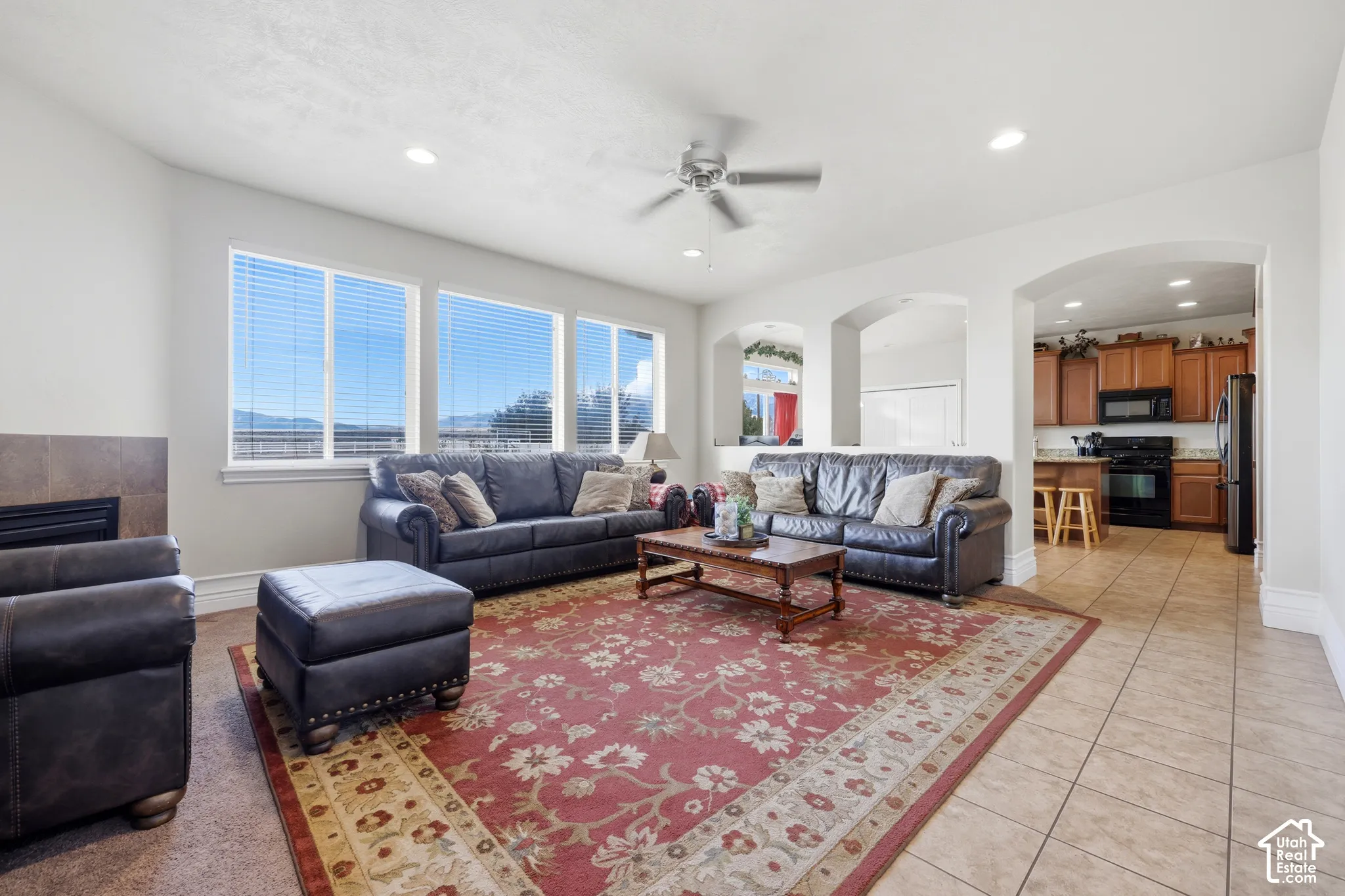Open-concept living space featuring ceramic tile flooring, arched wall openings, a tile-surround fireplace, recessed ceiling lighting, and a neutral color palette