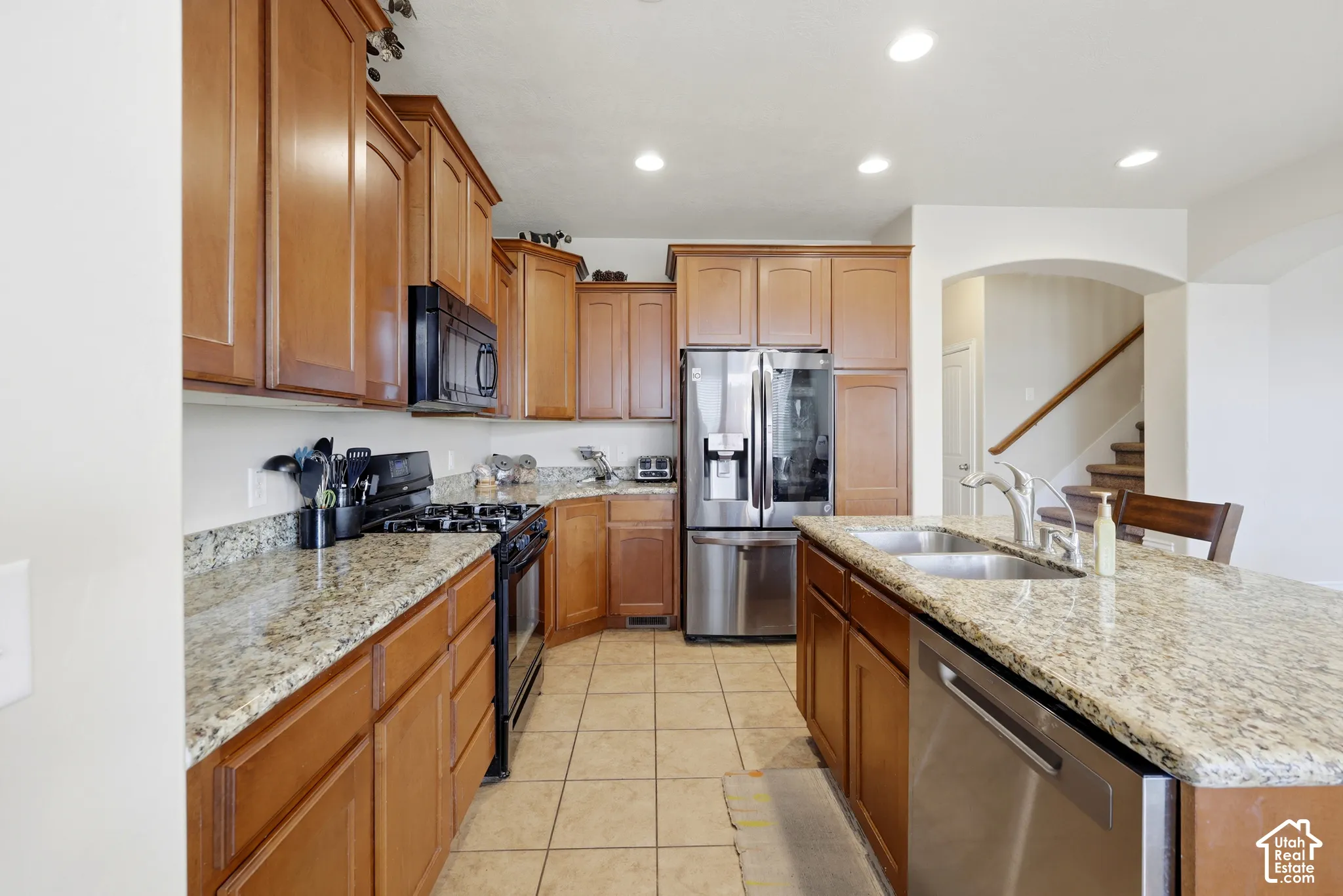 Kitchen featuring wood cabinetry, stone countertops, stainless steel appliances, a center island with a dual-basin sink, and recessed lighting