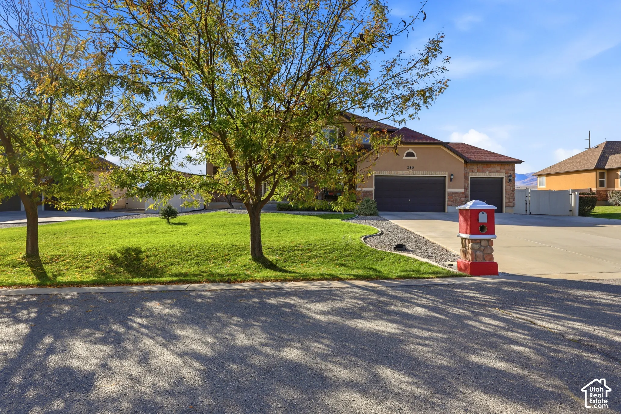 Exterior featuring a multi-car garage, brick and stucco facade, concrete driveway, stone-accented mailbox, and mature trees