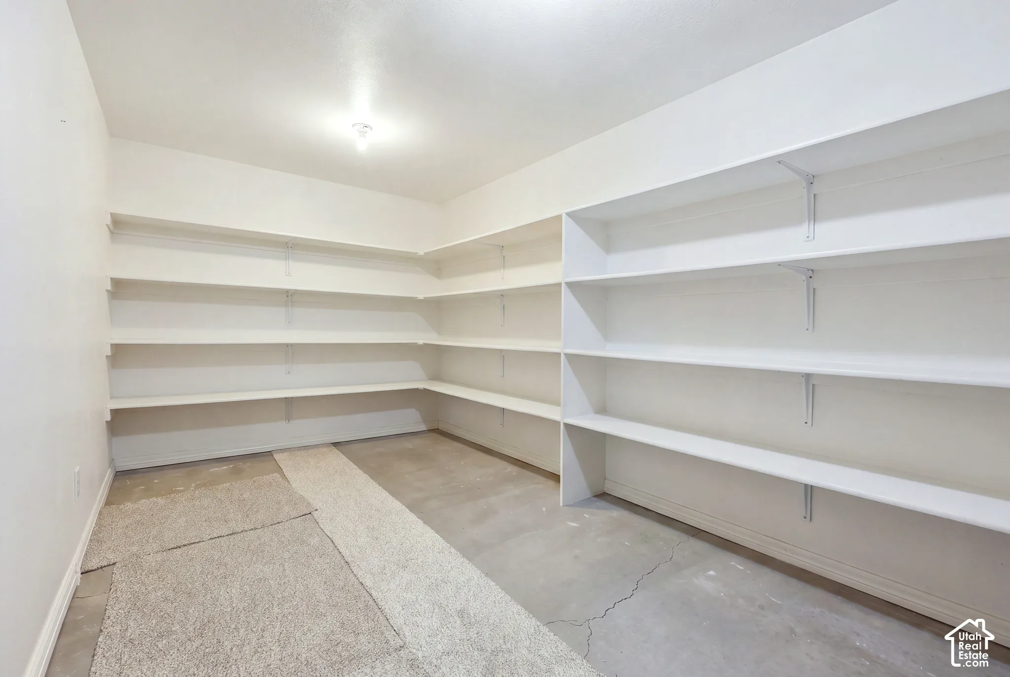 Storage area featuring wrap-around white shelving units and concrete flooring