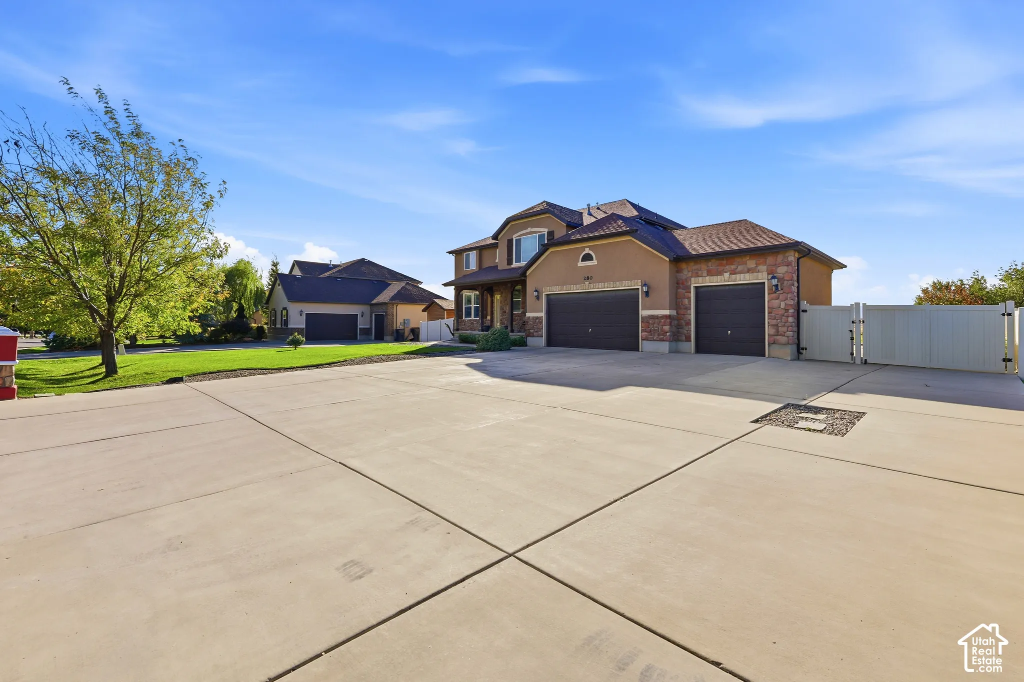 Stucco and stone veneer exterior featuring an attached three-car garage, expansive concrete driveway, and white vinyl perimeter fencing