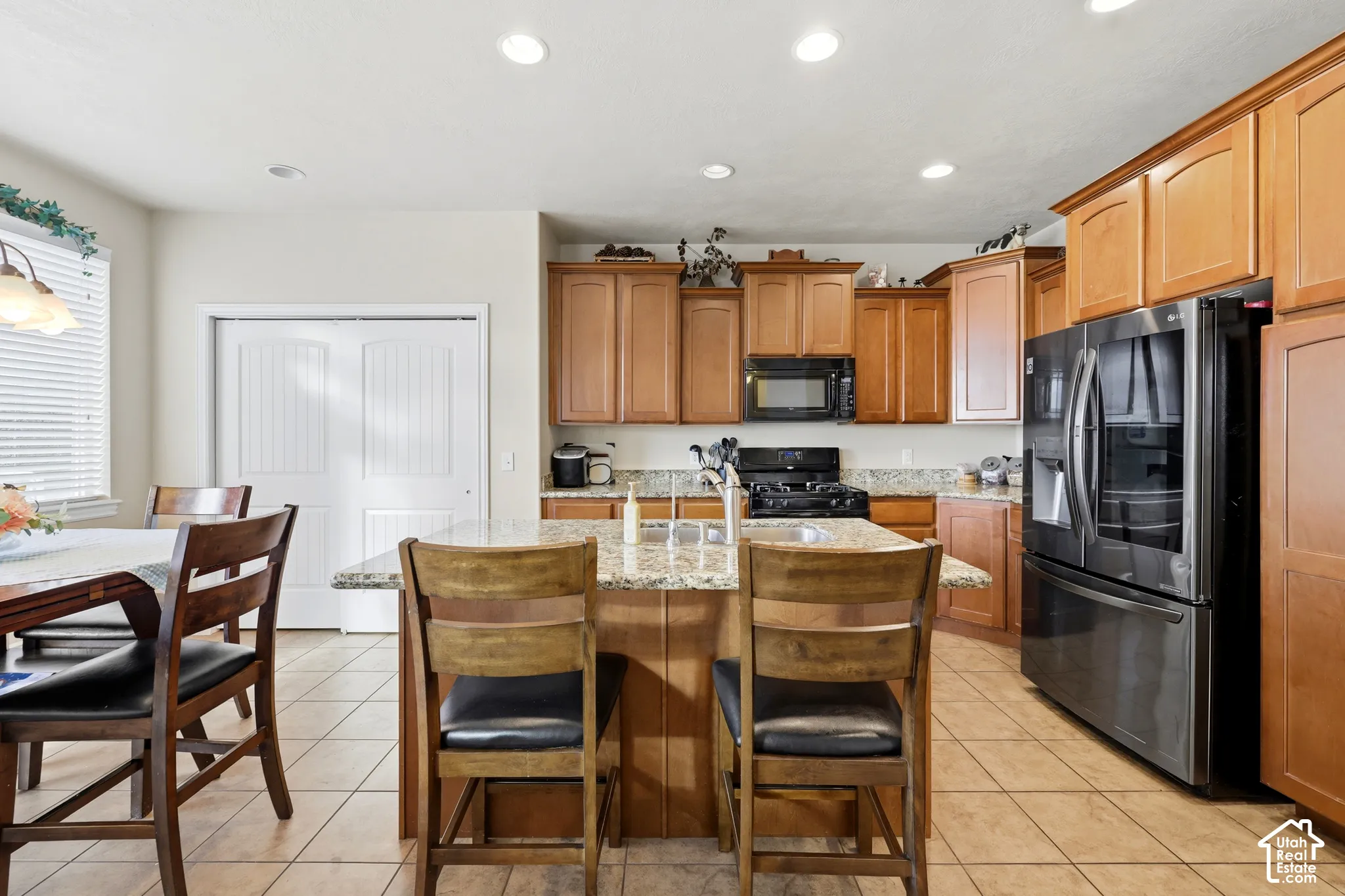 Kitchen featuring wood cabinetry, stone countertops, a center island with a built-in sink, recessed lighting, and tile flooring