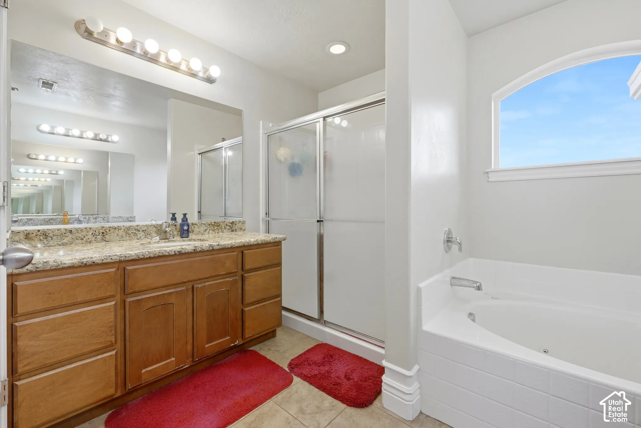Bathroom featuring a vanity with stone-finish countertop, shower with sliding glass doors, built-in soaking tub, and arched window