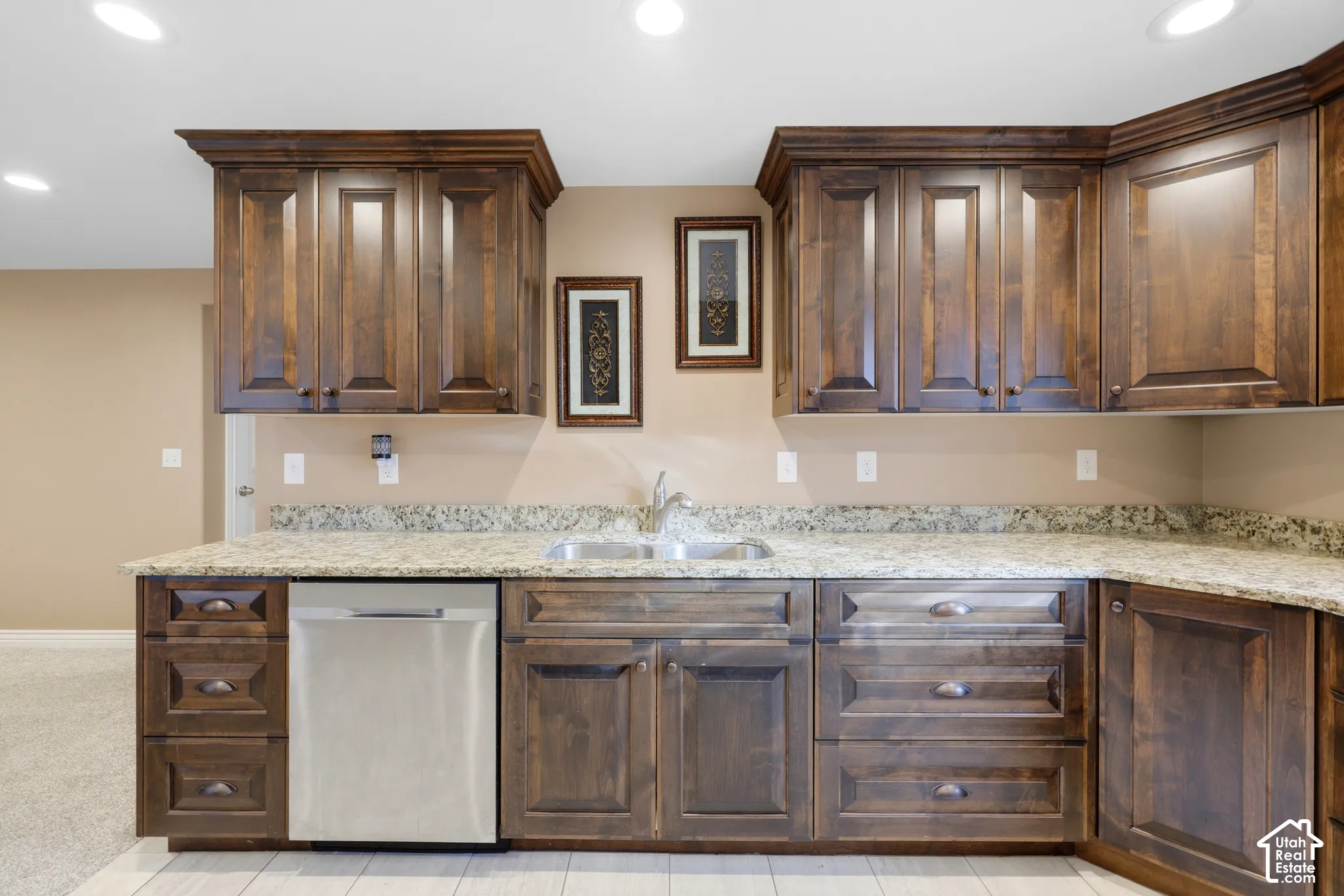 Dark-stained cabinetry with recessed-panel doors, stone-finish countertops, undermount double-basin stainless steel sink, integrated dishwasher, and recessed ceiling lighting
