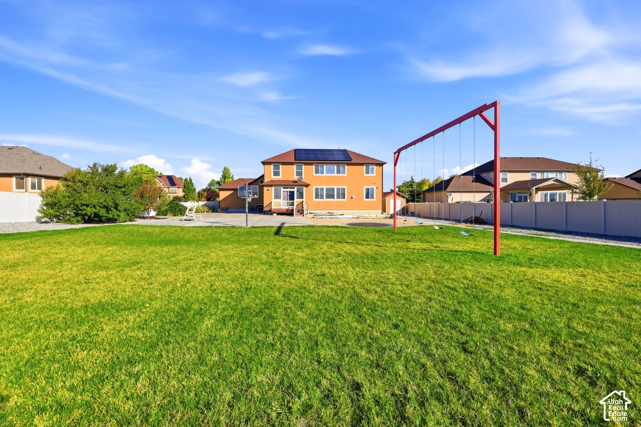 Expansive fenced backyard featuring a large grass lawn, solar panel array, and metal swing set