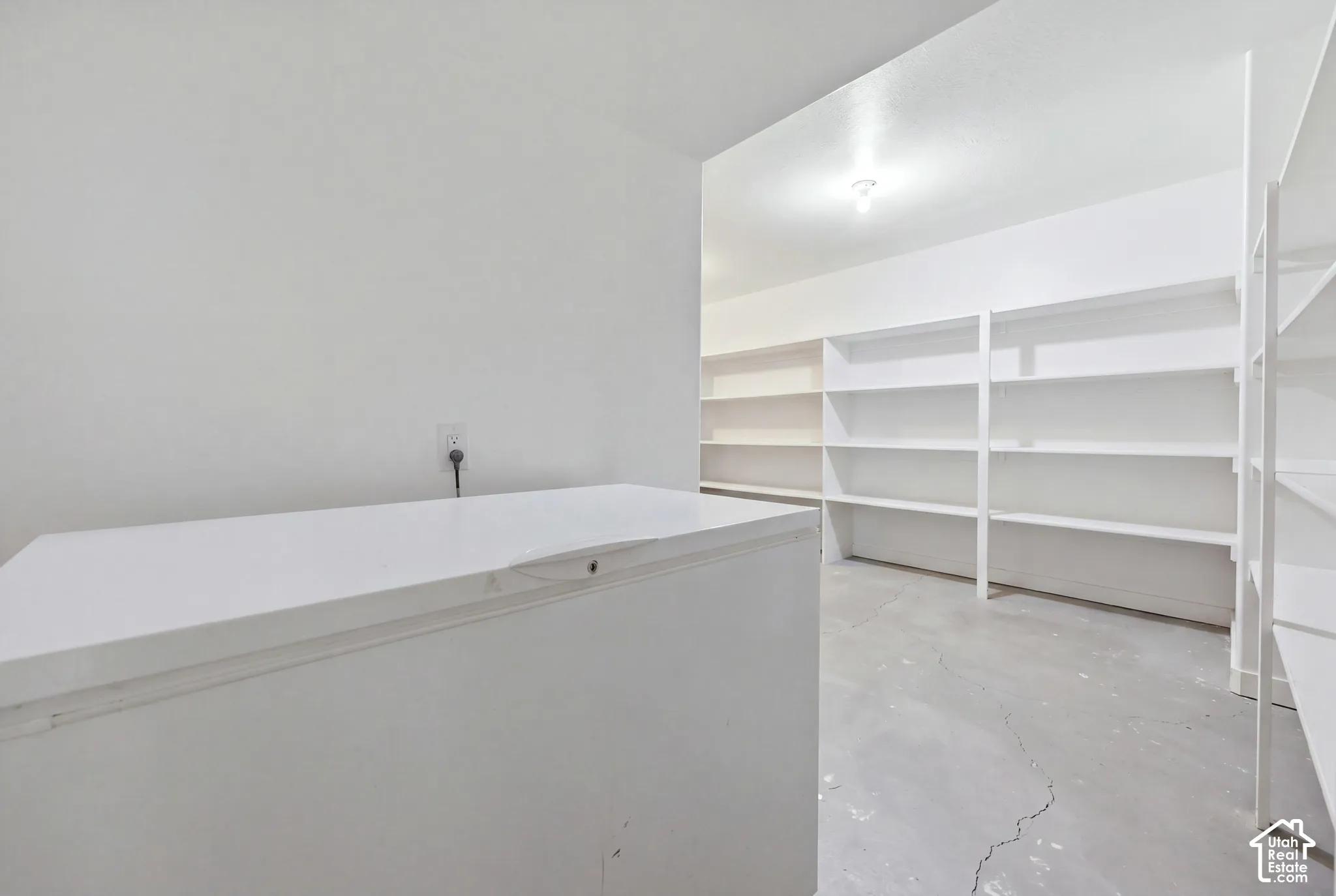 Storage area featuring built-in white shelving and concrete flooring