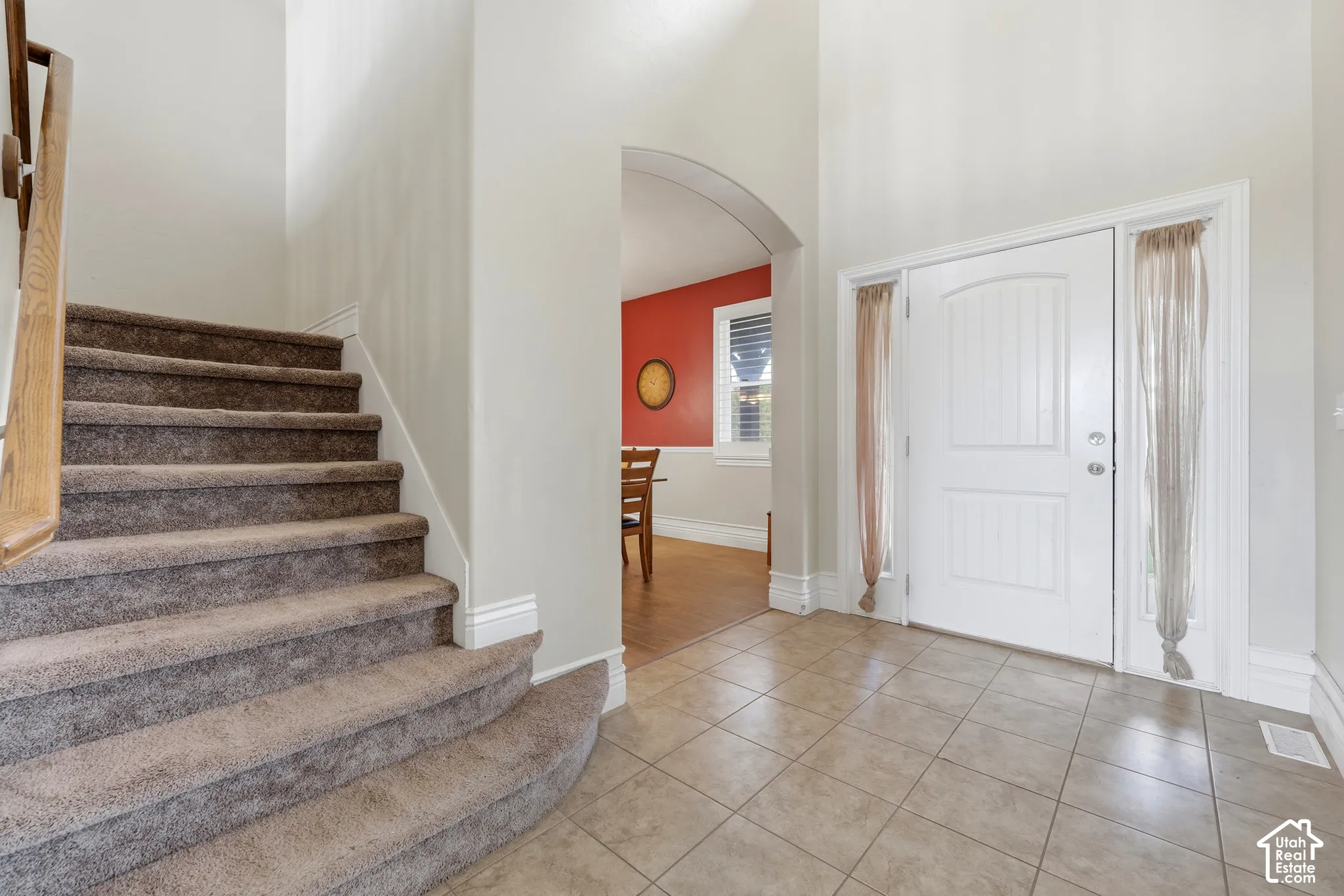 Foyer featuring ceramic tile flooring, a high ceiling, a wooden handrail, and an arched architectural opening