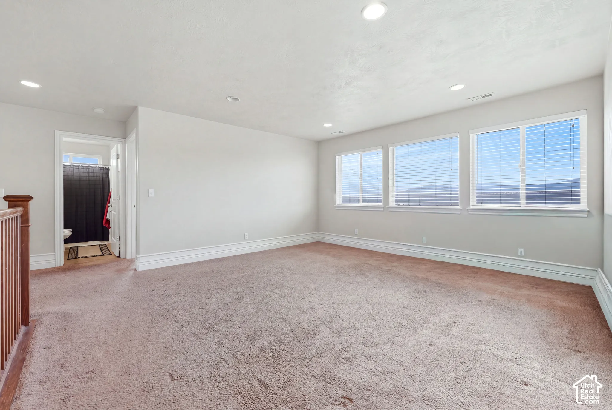 Spacious room featuring neutral carpeting, recessed ceiling lighting, and expansive windows with horizontal blinds