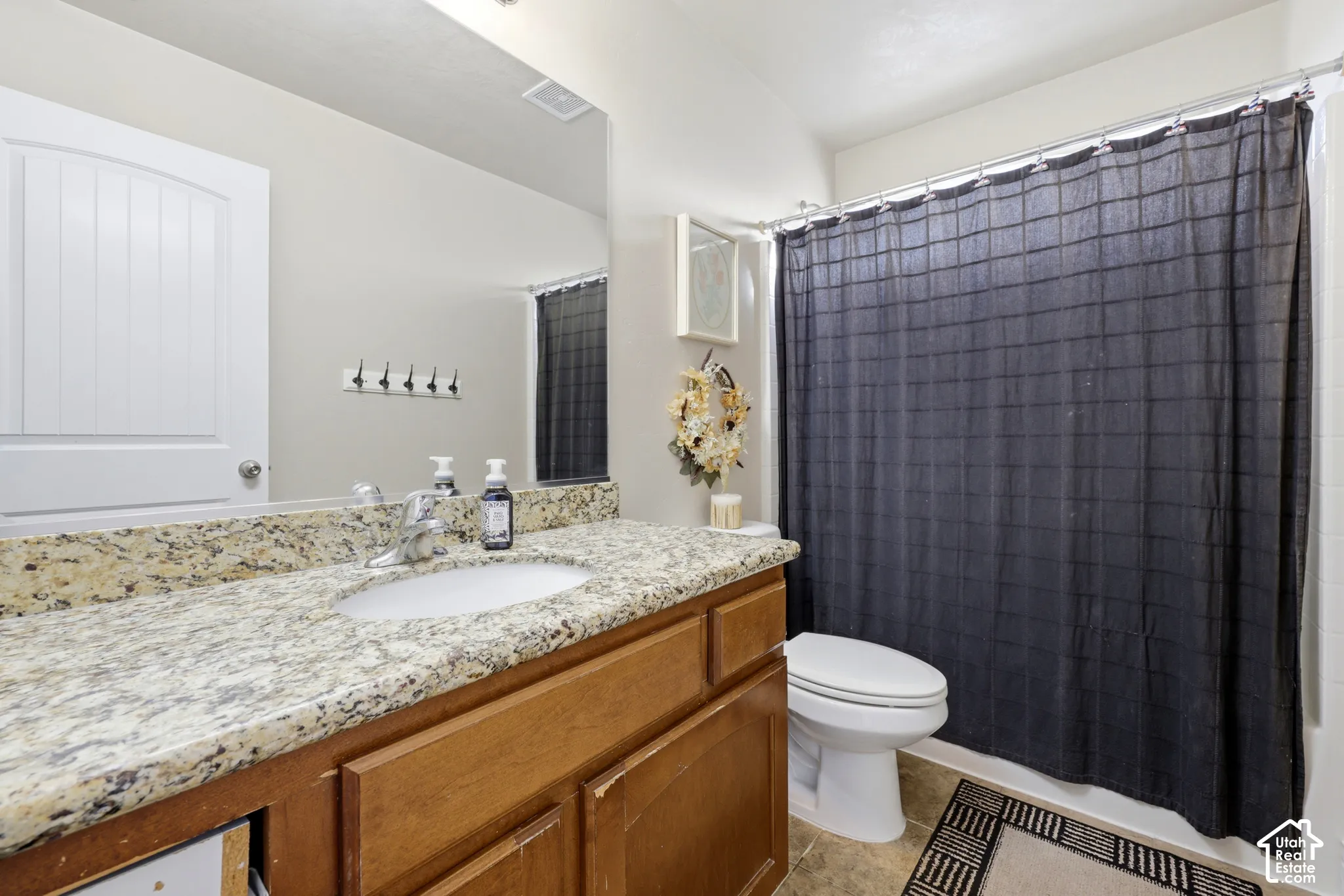 Stone-surface countertop, wood-finish vanity cabinetry, undermount oval sink, large wall-mounted mirror, and tile flooring
