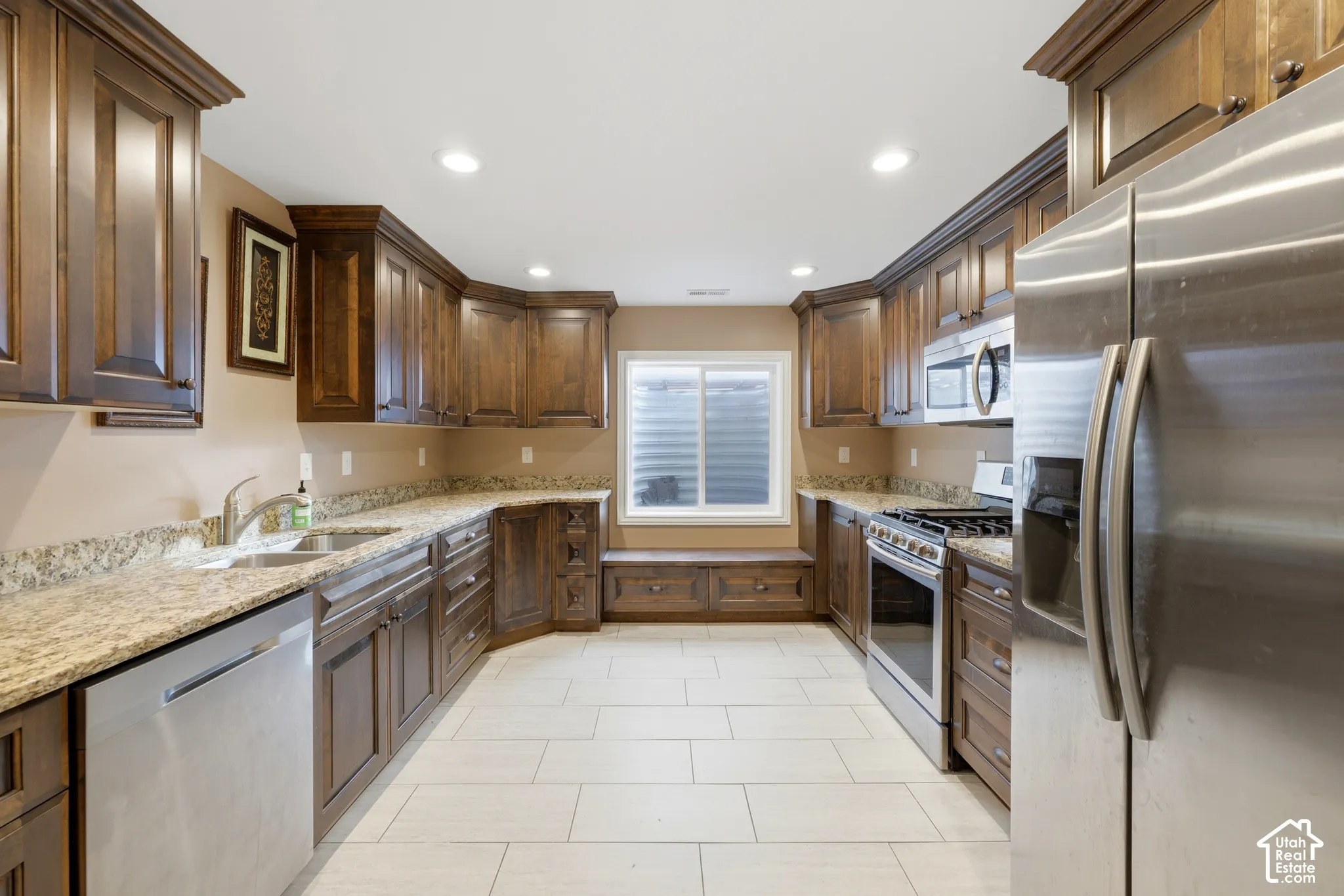Kitchen featuring dark-toned cabinetry, stone-finish countertops, stainless steel appliances, tile flooring, and built-in bench seating