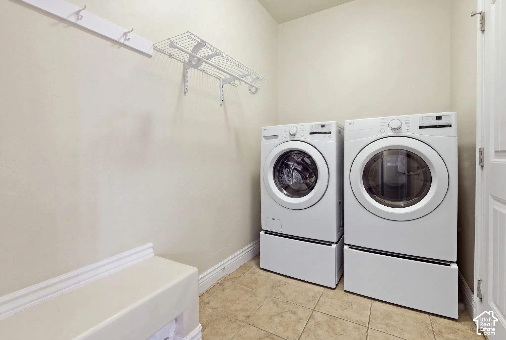 Utility room featuring tile flooring, white-finish wall-mounted cabinetry, integrated wall hooks, and dedicated space for laundry appliances