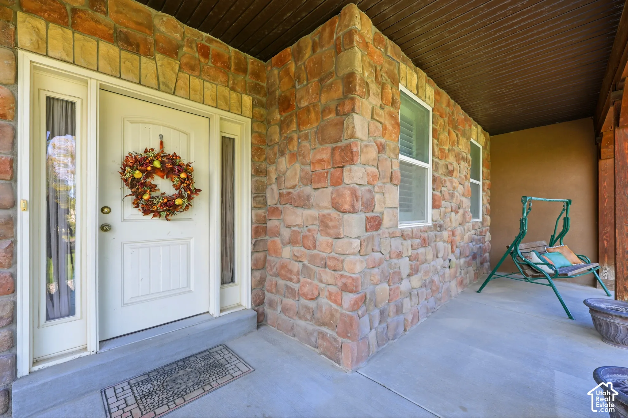 Covered front porch featuring natural stone facade, dual side-light windows, and a solid-core entry door