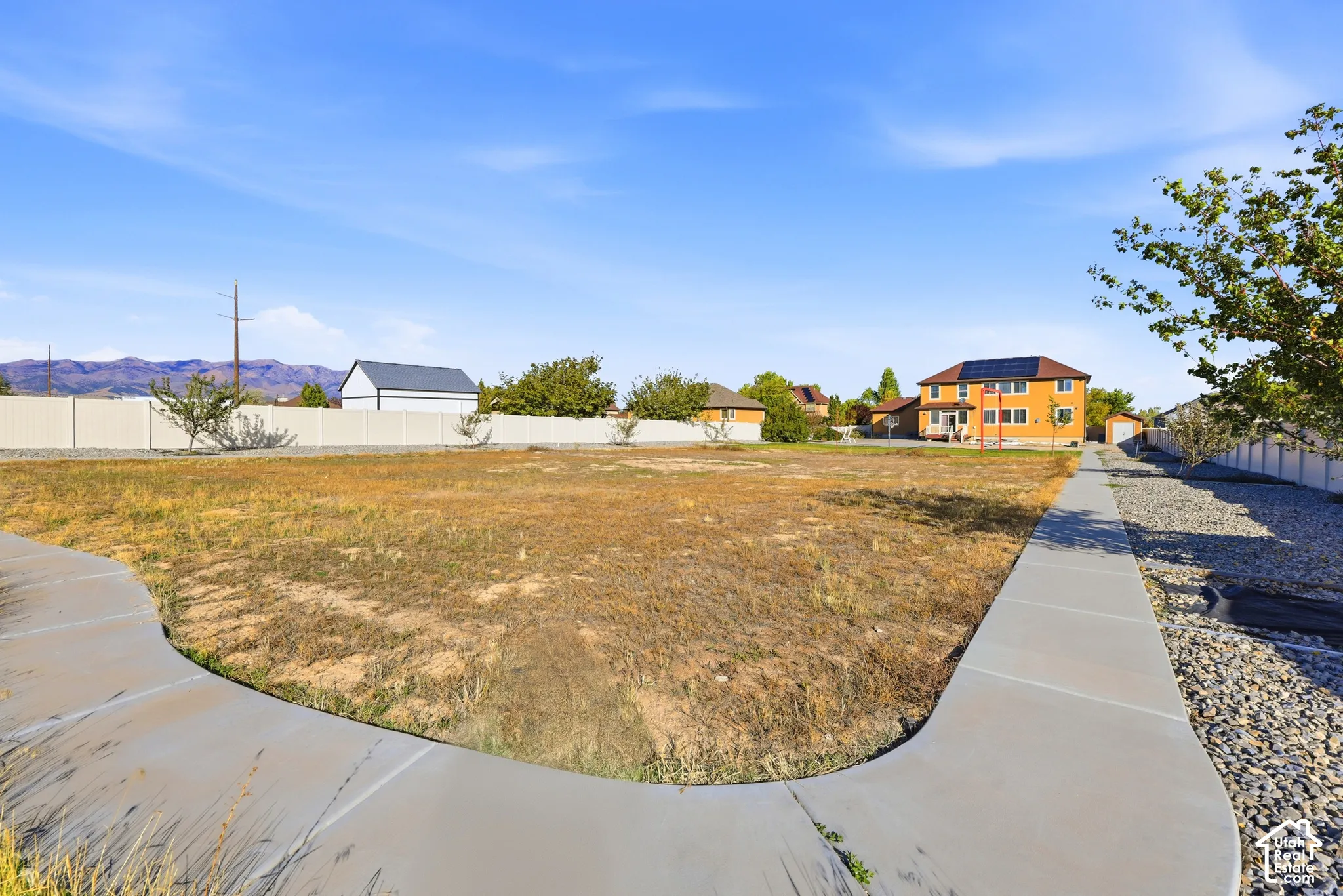 Expansive lot featuring a concrete walkway, perimeter vinyl fencing, and mountain backdrop