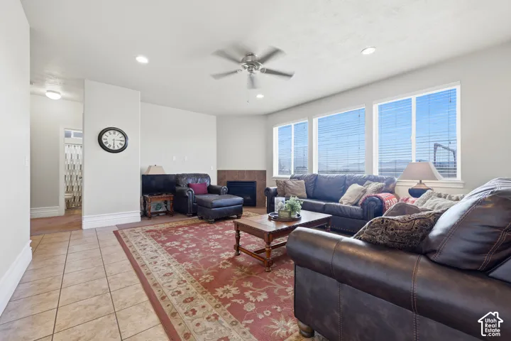 Neutral-toned living space featuring large windows, a corner fireplace with tile surround, recessed lighting, a ceiling fan, and ceramic tile flooring