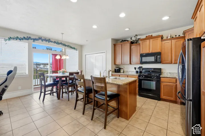 Kitchen featuring wood cabinetry, stone countertops, a center island with a sink, recessed lighting, and tile flooring