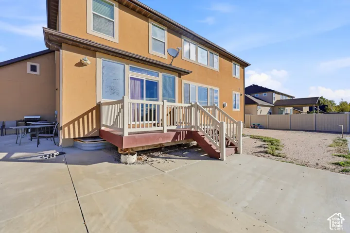 Stucco exterior featuring an elevated wood deck with railing and stairs, sliding glass doors, and a concrete patio