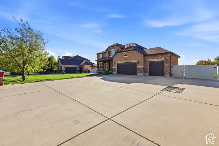 Stucco and stone veneer exterior featuring an attached three-car garage, expansive concrete driveway, and white vinyl perimeter fencing