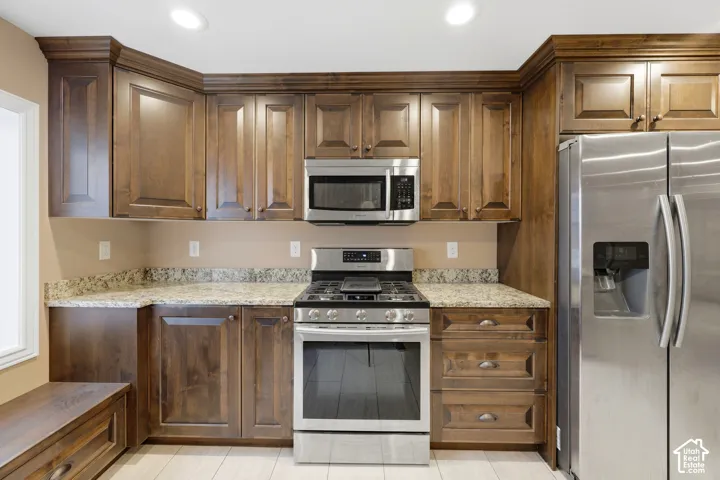 Kitchen featuring stained wood cabinetry, stone countertops, stainless steel appliances, recessed ceiling lighting, and tile flooring