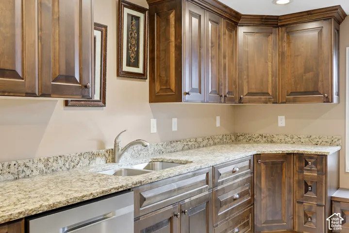 Kitchen featuring dark-stained wood cabinetry, stone countertops, dual-basin stainless steel sink with a high-arch faucet, and stainless steel dishwasher