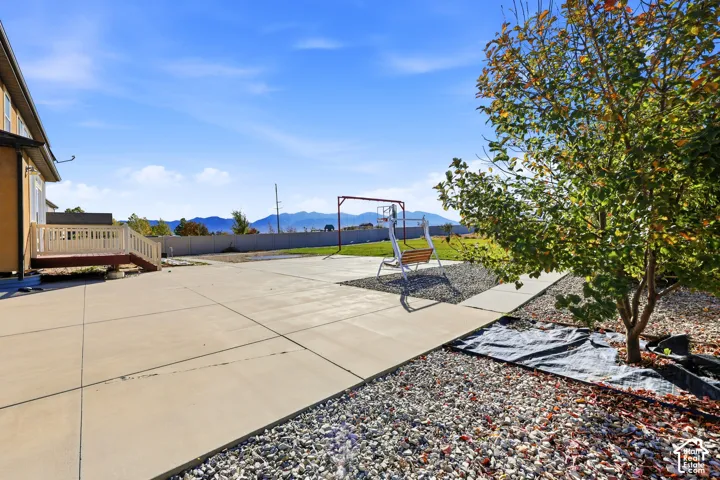 Spacious concrete patio, elevated wood deck with white railings, expansive lawn, gravel landscaping, and mountain backdrop