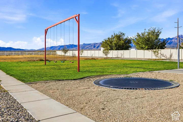 Expansive backyard featuring a grass lawn, gravel grounds, a metal swing set, an in-ground trampoline, and mountain scenery