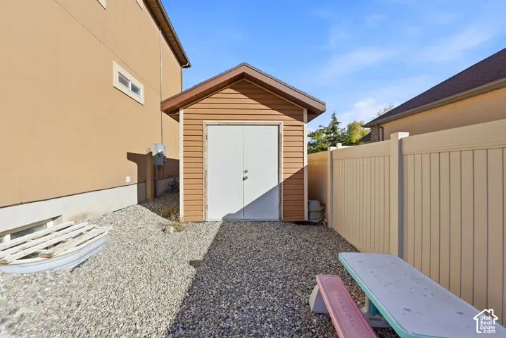 Detached storage shed featuring vinyl siding, a gable roofline, and double-entry doors, situated within a fenced exterior area with a gravel surface