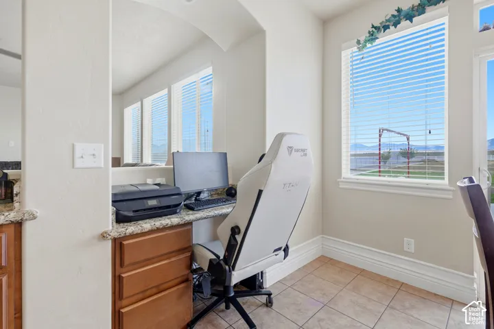 Built-in desk area with stone-composite countertop, natural wood cabinetry, large windows, and ceramic tile flooring