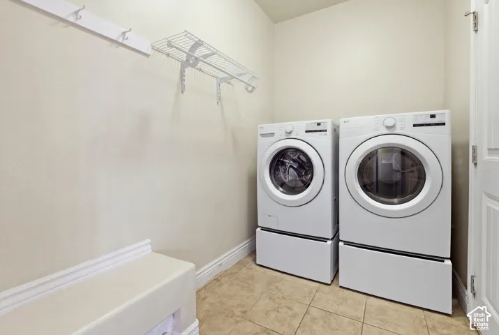 Utility room featuring tile flooring, white-finish wall-mounted cabinetry, integrated wall hooks, and dedicated space for laundry appliances