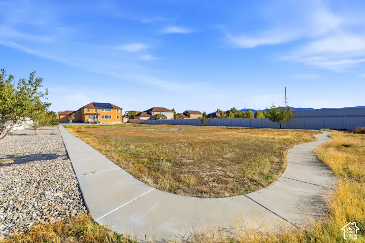 Expansive lot featuring a concrete walkway, perimeter vinyl fencing, gravel ground cover, and mountain silhouettes