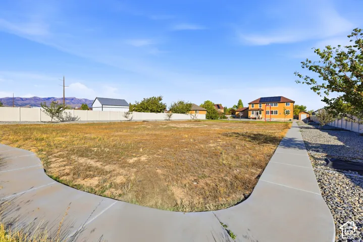 Expansive lot featuring a concrete walkway, perimeter vinyl fencing, and mountain backdrop
