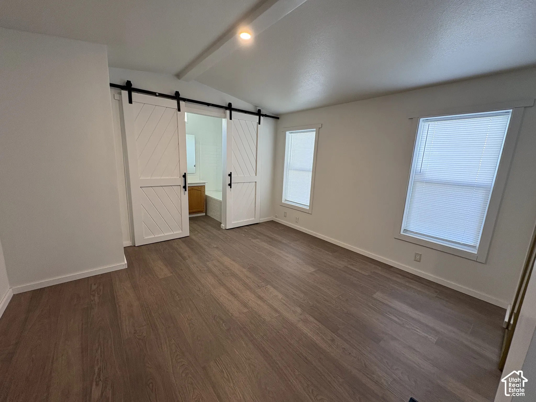Interior space featuring wood-finish flooring, sliding barn doors with matte black hardware, dual windows with integrated blinds, and recessed ceiling lighting