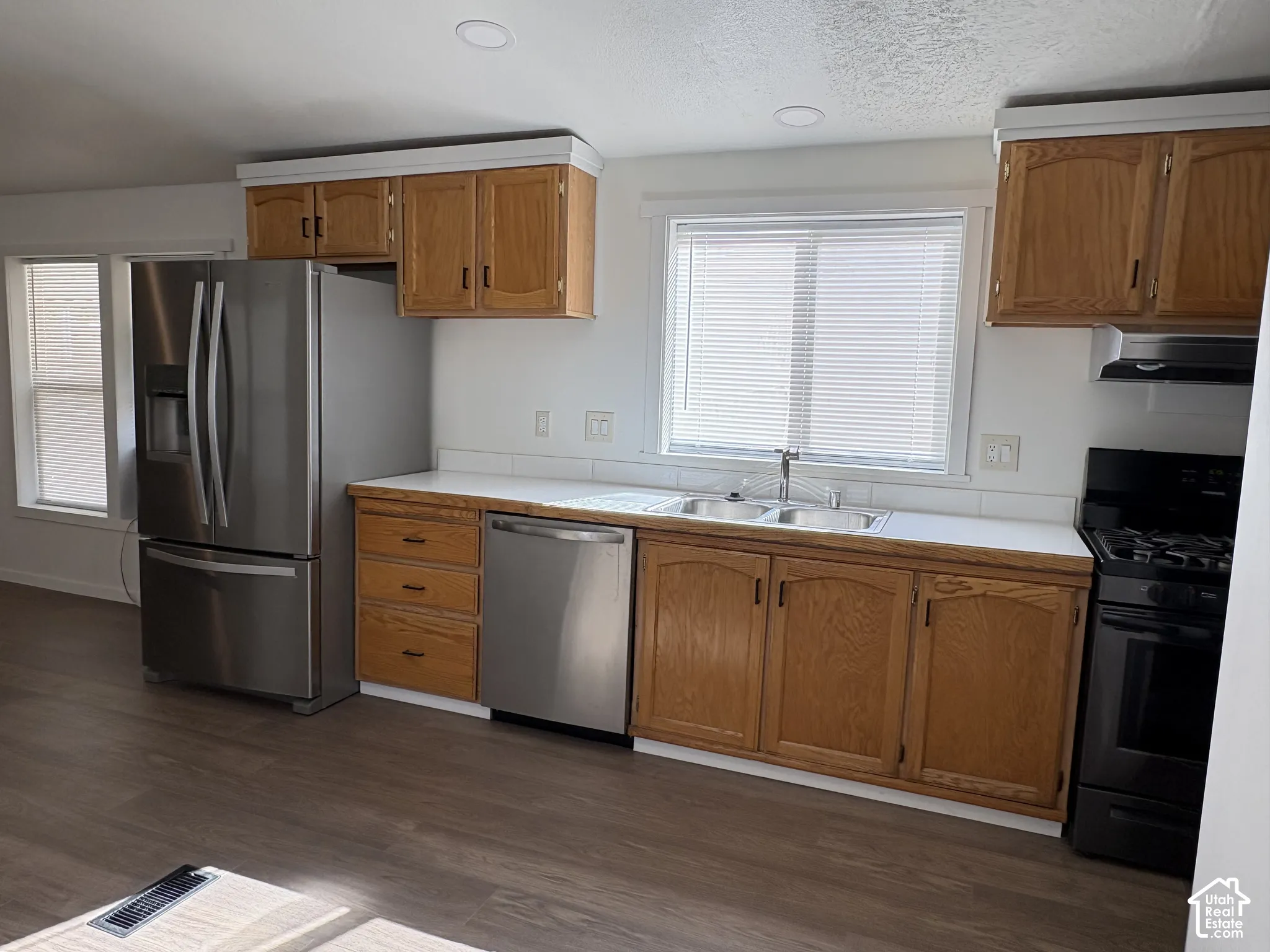 Kitchen featuring wood cabinetry, stainless steel appliances, white solid-surface countertops, dual-basin sink, and recessed lighting
