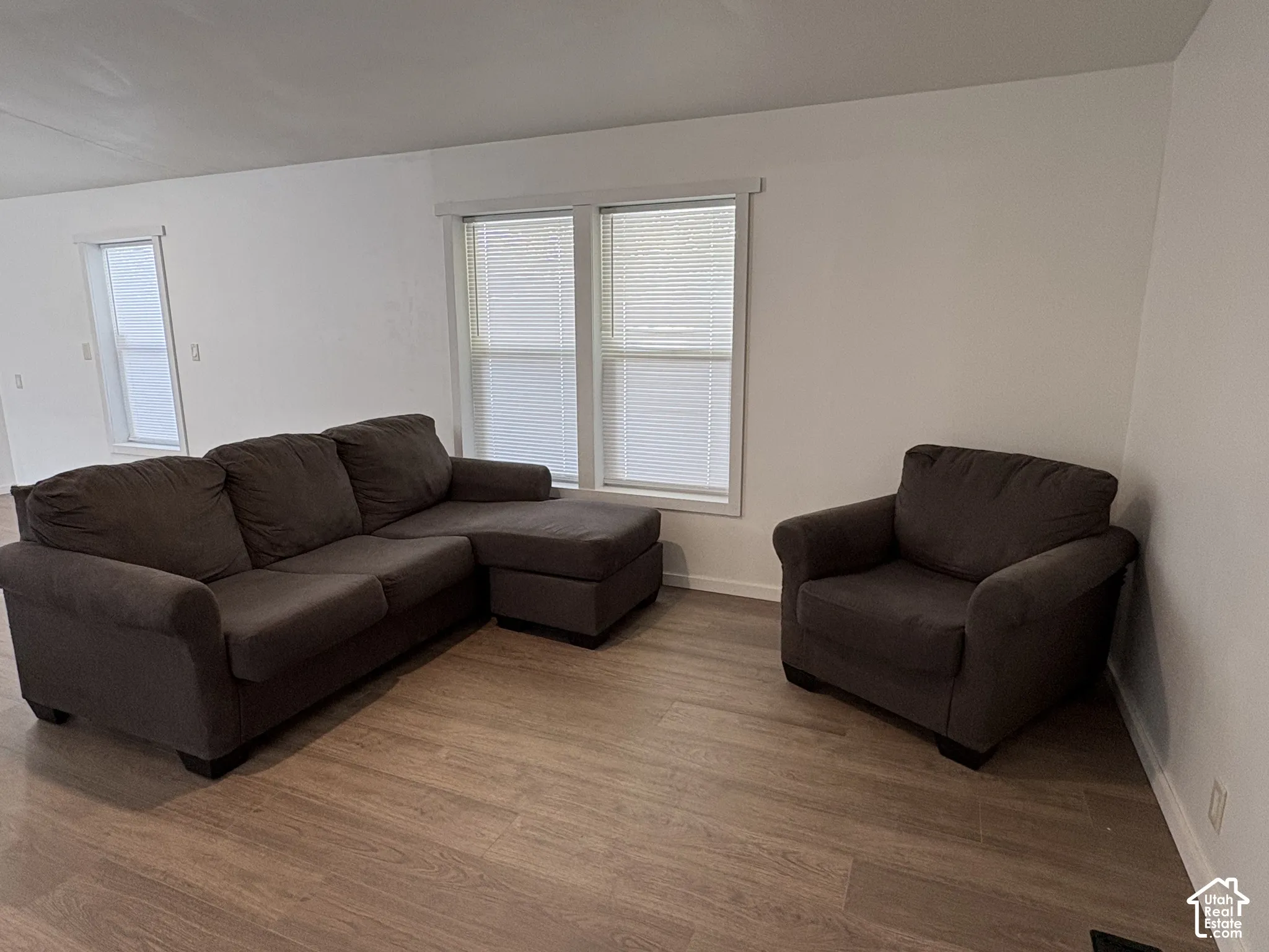Neutral interior featuring wood-finish flooring, white walls, and multiple double-pane windows with horizontal blinds