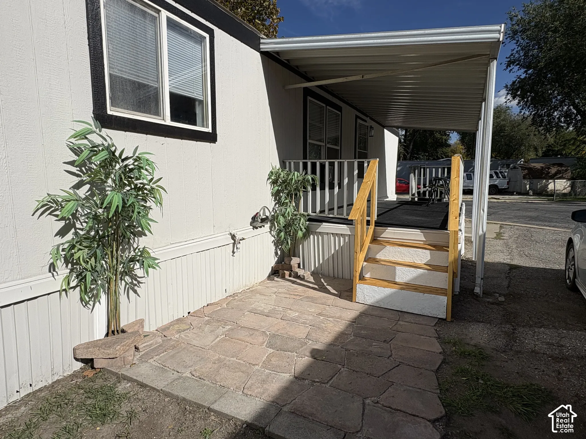 Exterior featuring a stone-paver patio, a covered carport, and a raised porch with white railings and wood-finish steps