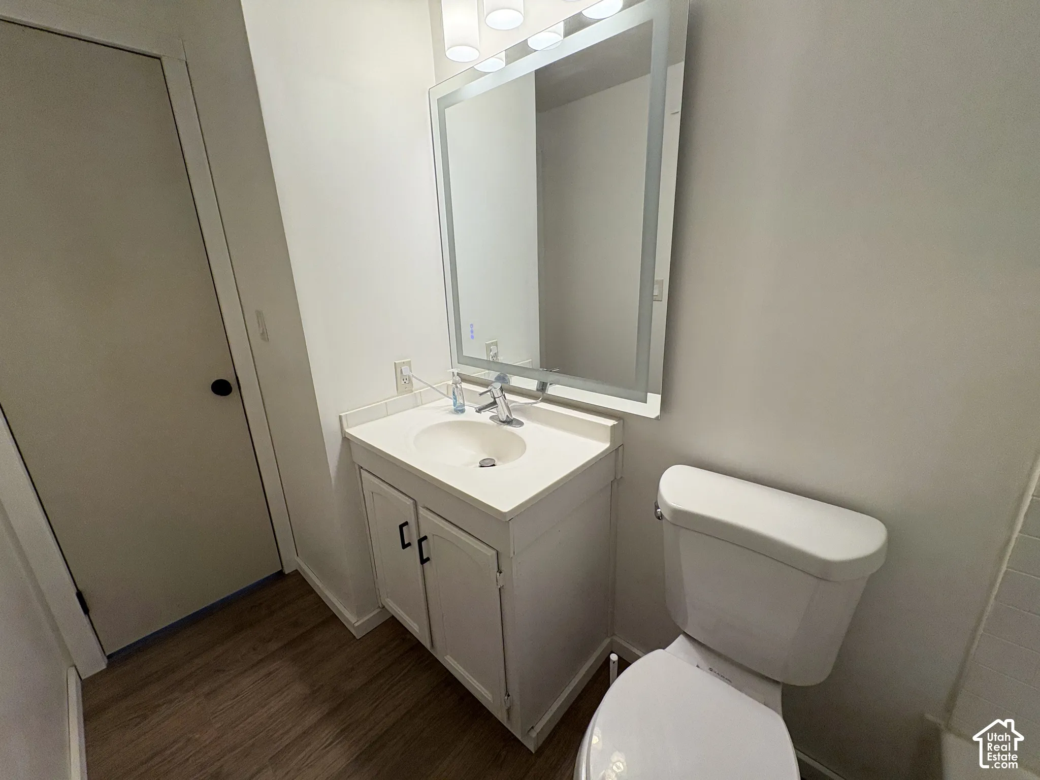Bathroom featuring a wood-finish floor, a vanity with a white countertop and basin, an integrated rectangular LED-backlit mirror, and chrome finish hardware