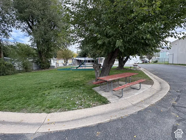 Common area featuring a grass lawn, mature trees, concrete pad, and playground equipment