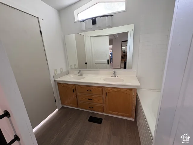 Double vanity featuring wood-finish cabinetry, a large wall-mounted mirror, transom window, and wood-finish flooring